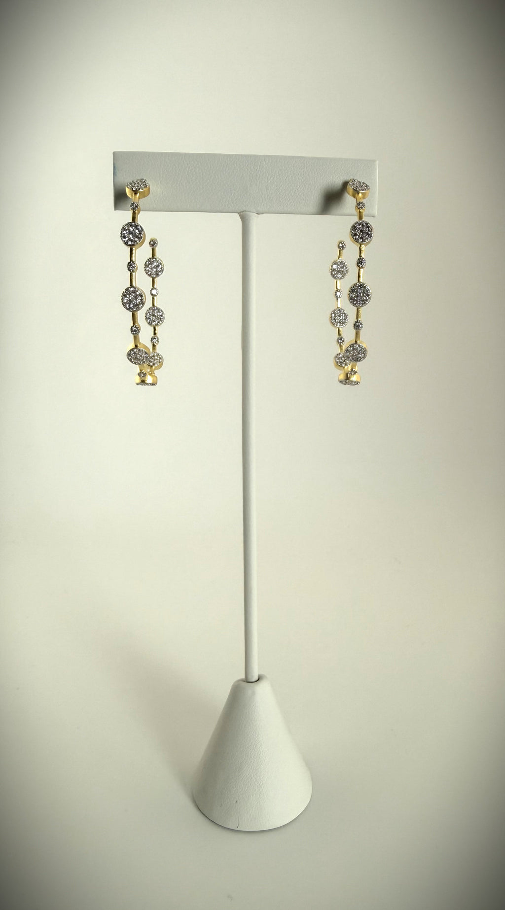 Elegant gold pavé diamond drop earrings showcased on a white stand