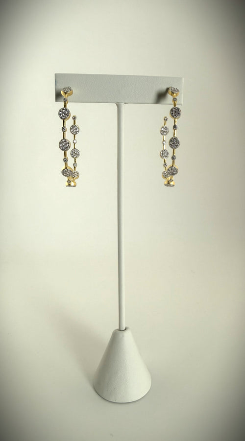 Elegant gold pavé diamond drop earrings showcased on a white stand