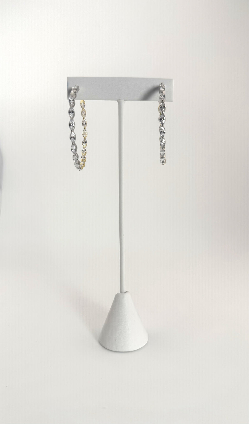 Two-tone silver and gold diamond hoop earrings on a white jewelry stand