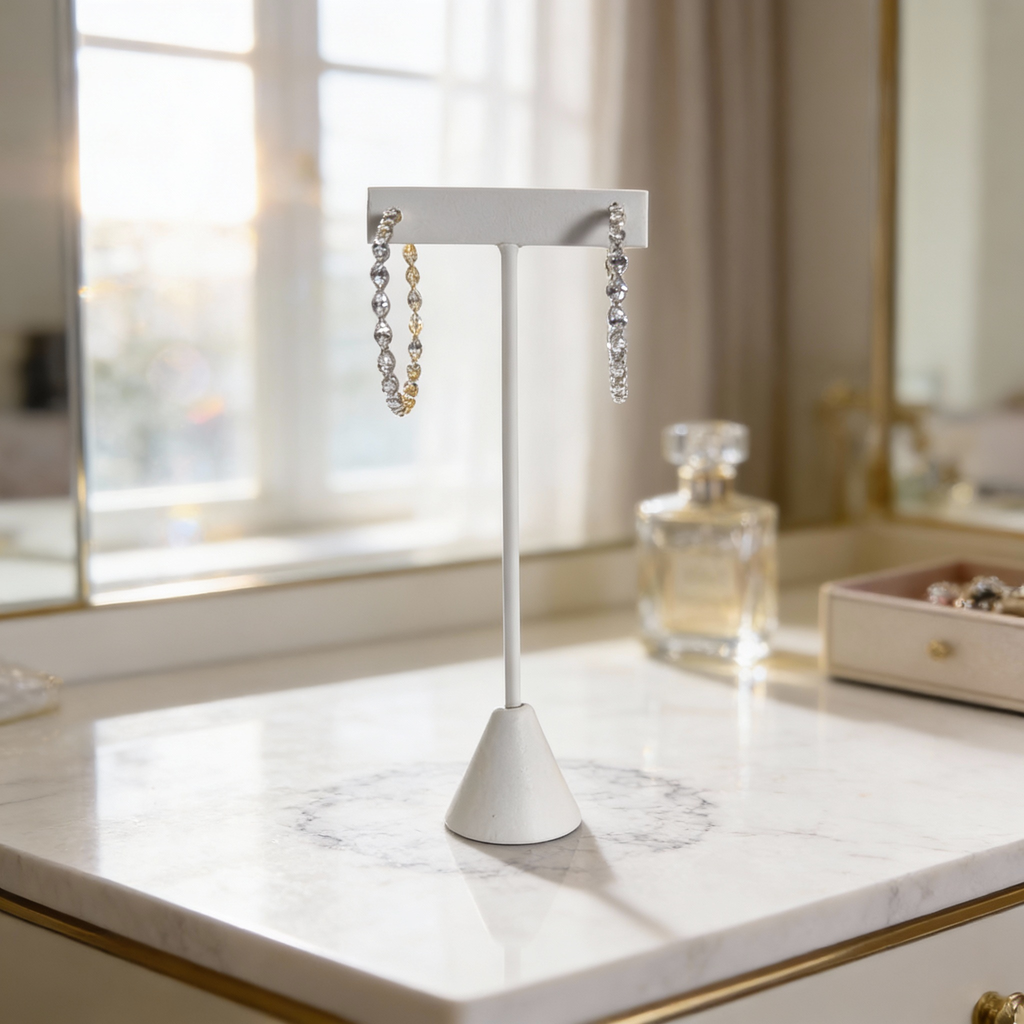 Silver and gold diamond hoop earrings displayed on a white stand atop a marble surface with soft window light.