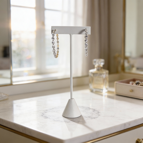Silver and gold diamond hoop earrings displayed on a white stand atop a marble surface with soft window light.