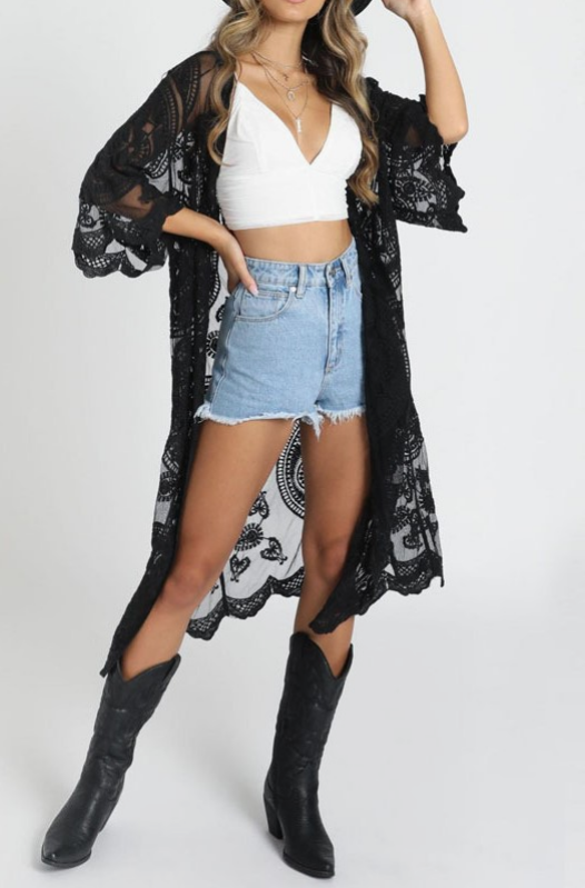 Woman wearing a black lace kimono, white top, denim shorts, and black boots on a white background