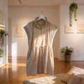 Beige dress with blue stripes hanging in a room with wooden floor and plants.