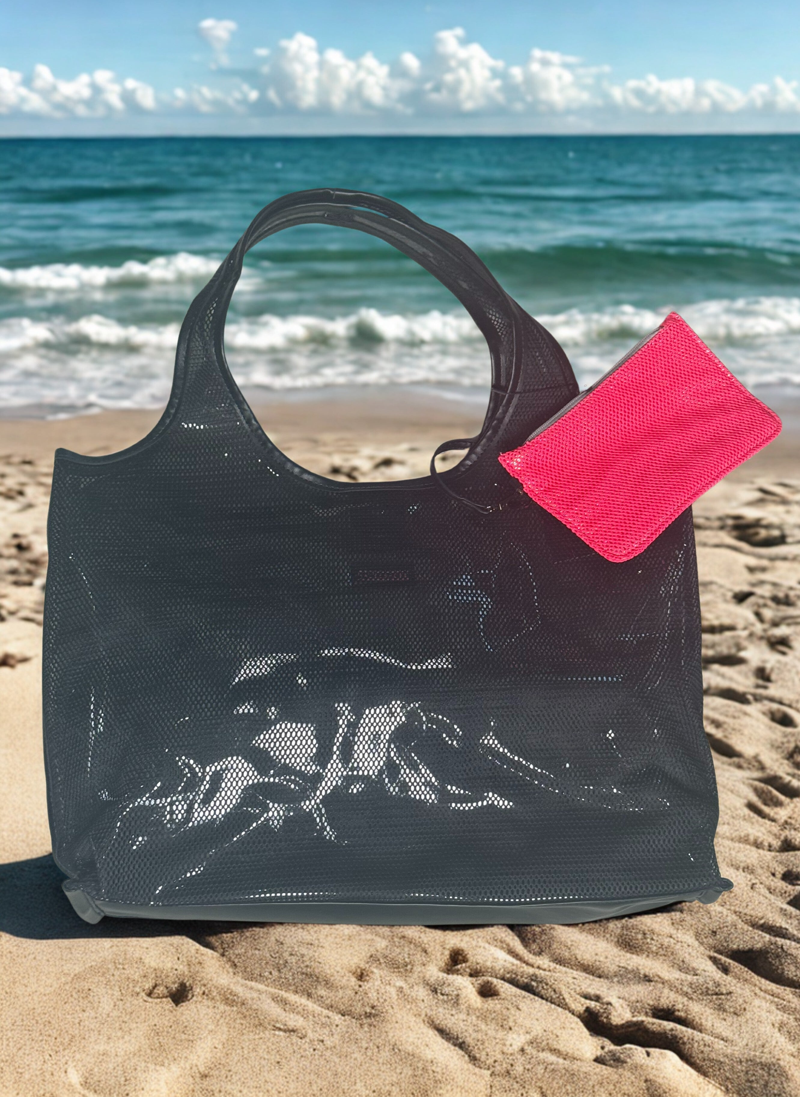 Black mesh tote bag lined with plastic with a pink tag on a sandy beach with ocean in the background