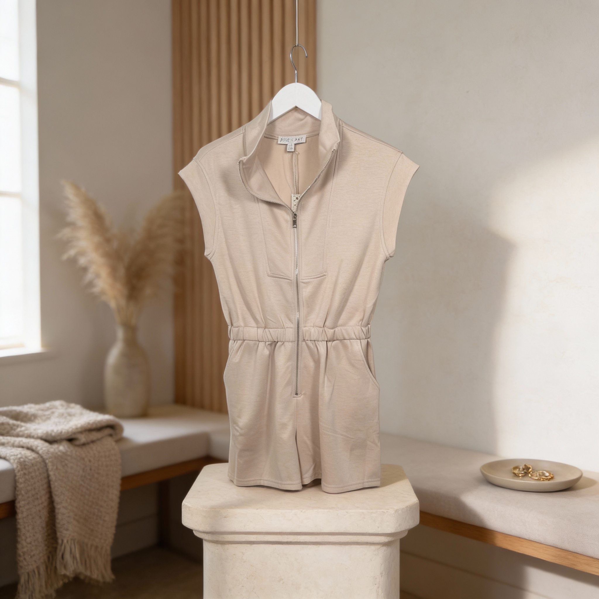 Women’s light taupe sleeveless half-zip romper featuring an elastic waist, soft knit fabric, and easy resort-ready silhouette