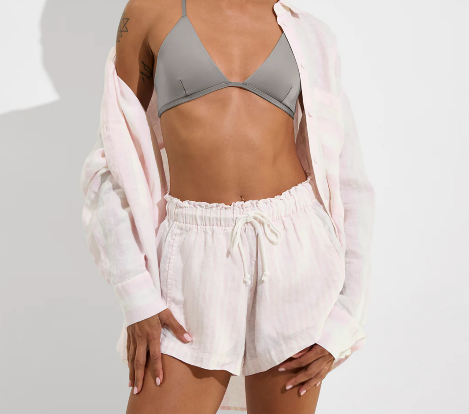 Person wearing a gray bikini top and white shorts with a light pink cover-up on a white background