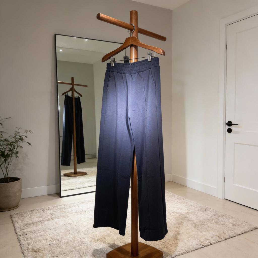 Navy pants hanging on a wooden stand in a room with a mirror and plant.