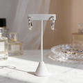Silver hoop earrings on a white stand with a blurred background of perfume bottles and jewelry.