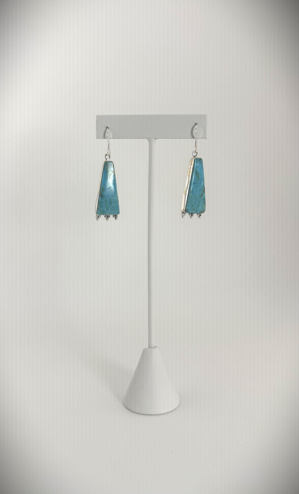 Sterling silver turquoise triangle drop earrings displayed on a jewelry stand