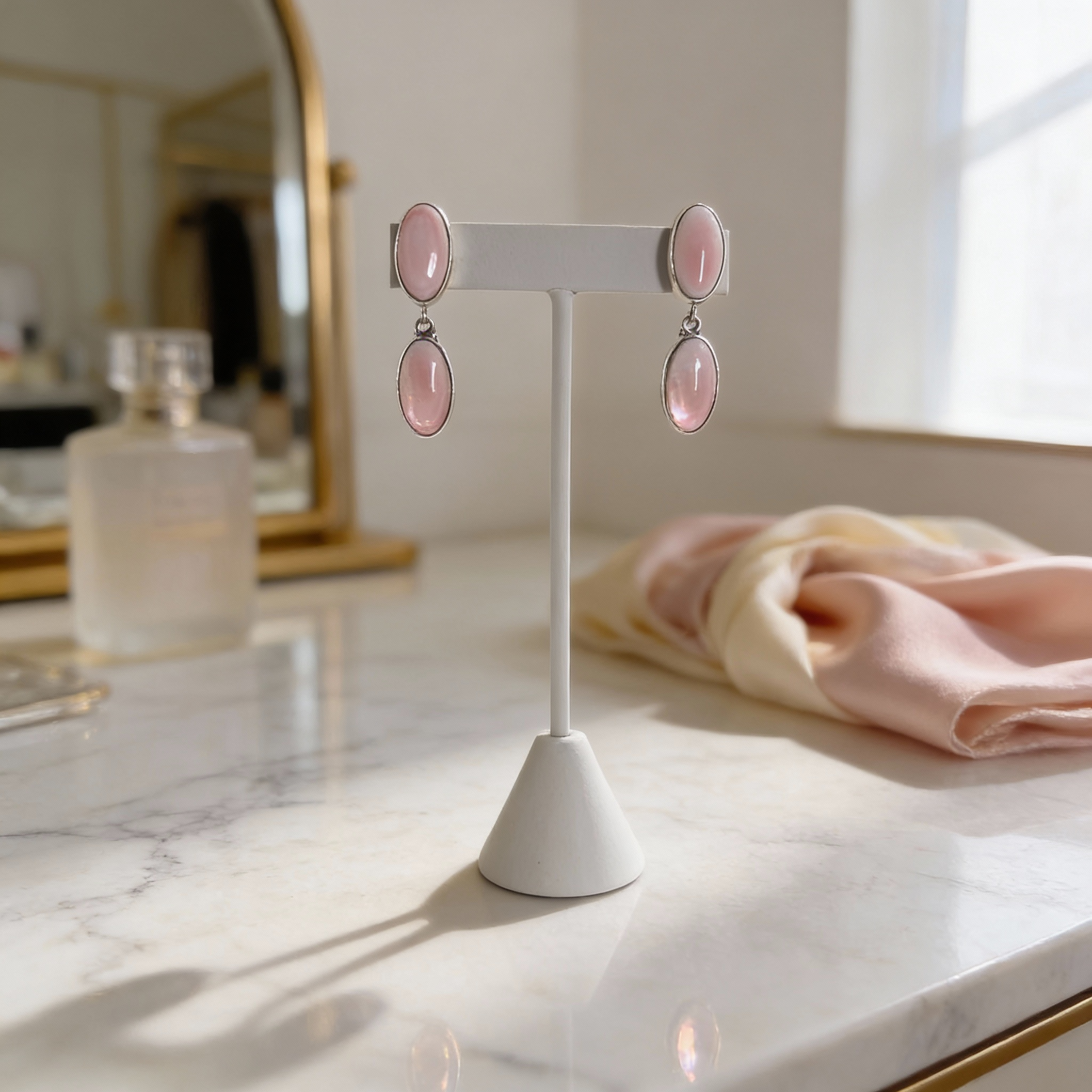 Sterling silver pink stone dangle earrings displayed on a white jewelry stand.