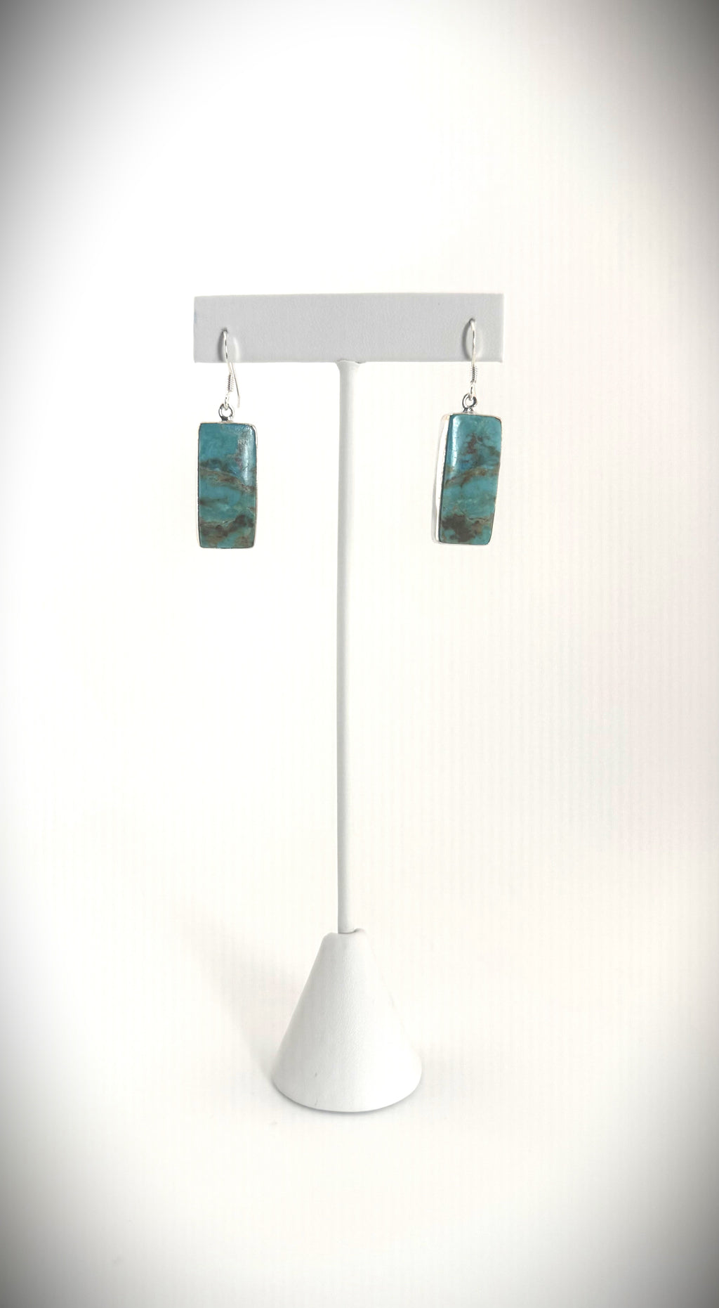 Sterling silver turquoise rectangular drop earrings with natural stone veining on a modern display stand.